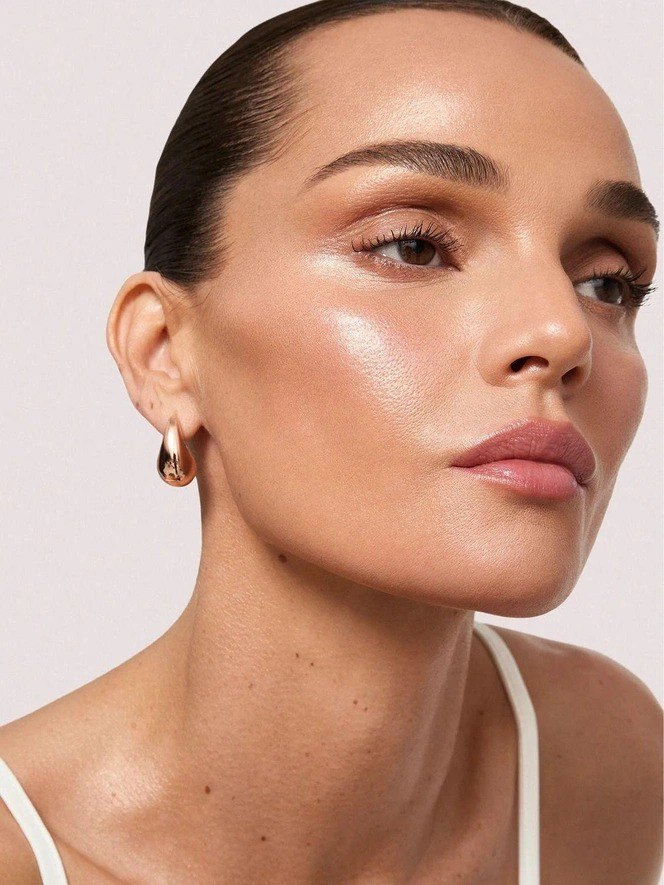 Крупный план лица модели с сияющим тоном кожи: подчеркнуты скулы, ровная текстура и аккуратный лёгкий мейкап для праздничного образа.