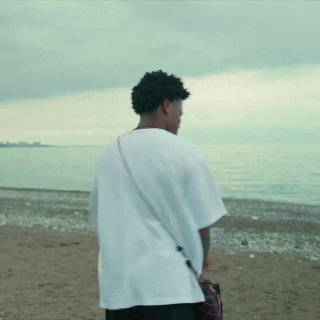 Мужчина в белой футболке стоит на берегу моря на каменистом пляже, смотрит в сторону воды — кадр из тревел‑видео об Абхазии.