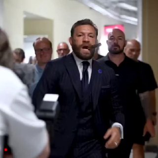 Мужчина в деловом костюме идёт по коридору среди людей; эмоциональная сцена, возможный участник торгового или медиасобытия, без идентификации личности.