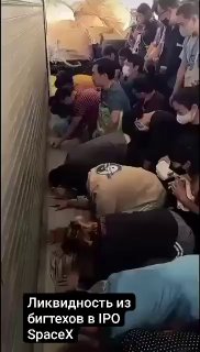 Вертикальное превью-видео: группа людей в плотной толпе в узком помещении, многие с телефонами; на кадре виден текст о ликвидности и IPO.
