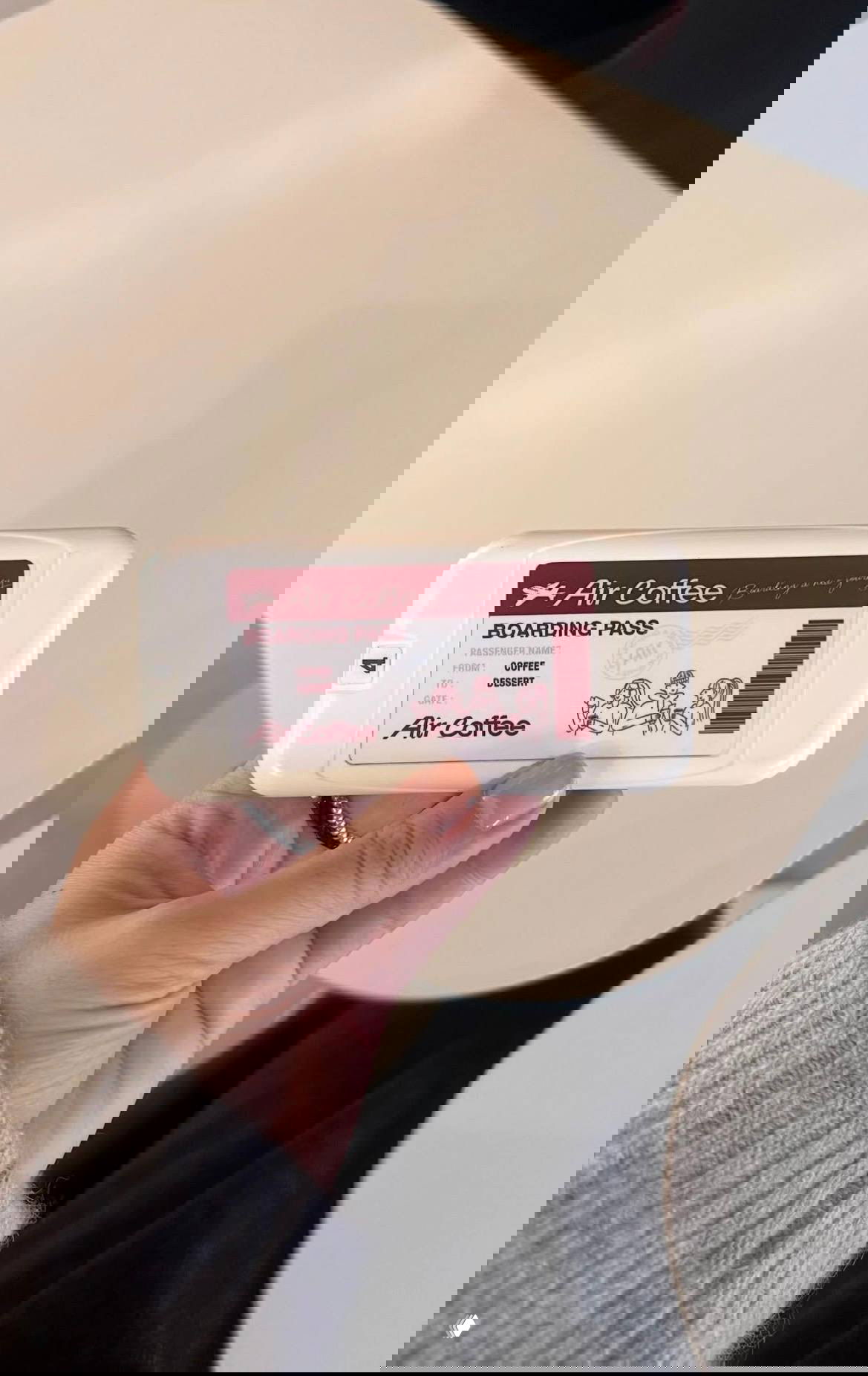 Рука держит пластиковый «boarding pass» от Air Coffee с надписями Boarding Pass, From: Coffee и иллюстрацией — сувенирный пропуск кофейни в самолёте.