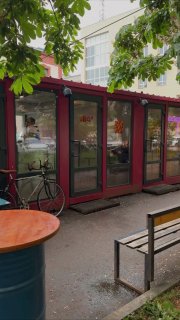 Фасад небольшой красной уличной закусочной в Санкт-Петербурге: модульная кабина с витринами, велосипед у входа и скамейка.