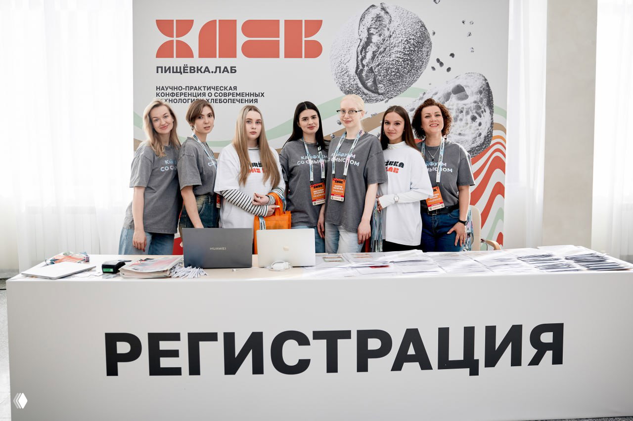 Регистрационная стойка конференции «Пищёвка.ЛАБ: Хлеб»: команда организаторов у брендового баннера и материалы для участников.