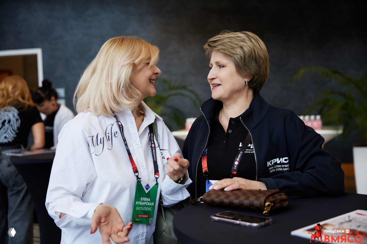 Две участницы обсуждают вопросы отрасли у фуршетного столика, видны бейджи и фирменные элементы конференции ВМЯСО — атмосфера делового общения.