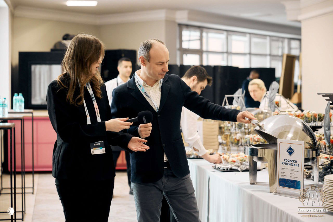 Посетитель берет угощение с фуршетного стола на Ассортиматике: шведский стол с подогреваемыми блюдами и маркированными закусками.