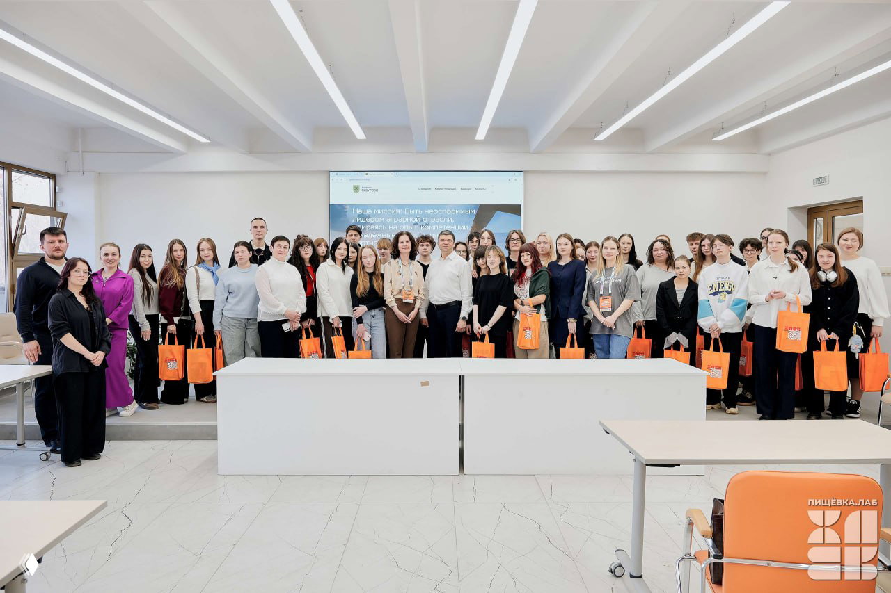 Групповое фото участников Пищёвка.ЛАБ в Тимирязевской академии: люди в аудитории с оранжевыми сумками и бейджами, встреча.