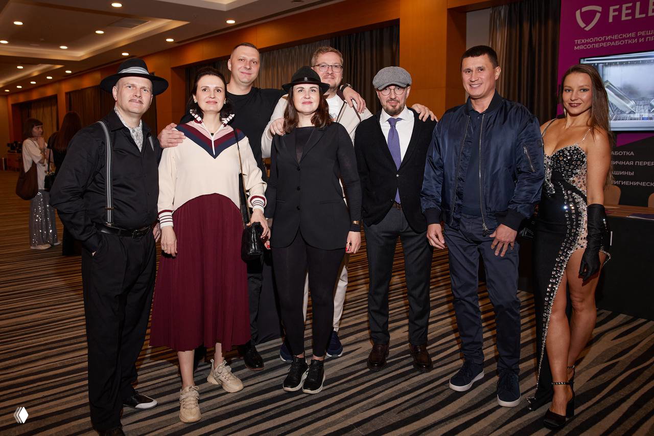 Группа участников позирует для общего фото в коридоре мероприятия: сочетание делового и креативного стиля одежды, дружеская атмосфера.