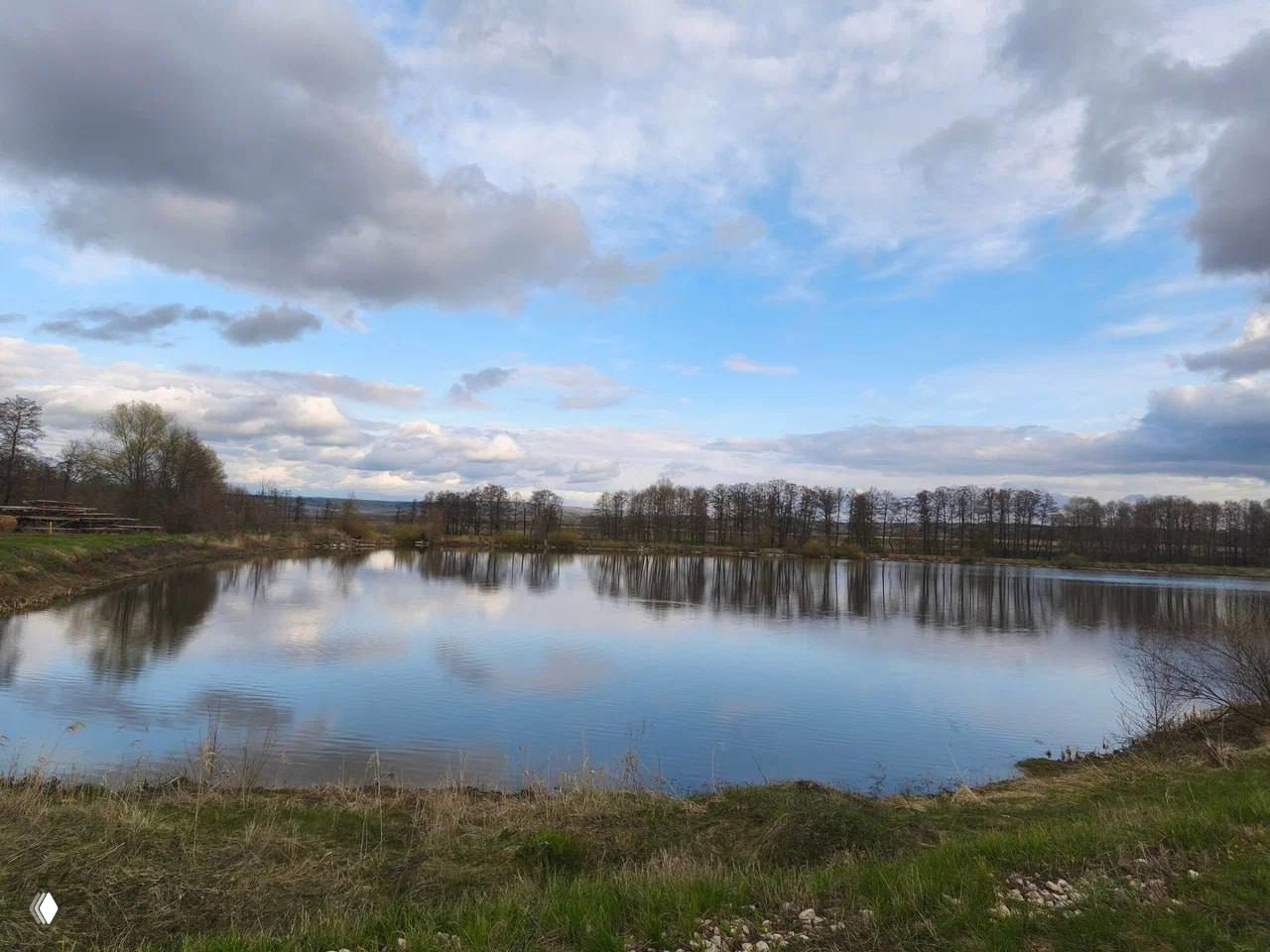 Озеро с отражением неба и берёзовой полосой, спокойная водная гладь и лесистые берега — идеальное место для купания и прогулок.