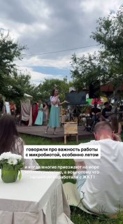 Выступление на фестивале ЗОЖ у реки: лектор на сцене, публика сидит на траве, вокруг деревья и палатки, тёплая летняя атмосфера.