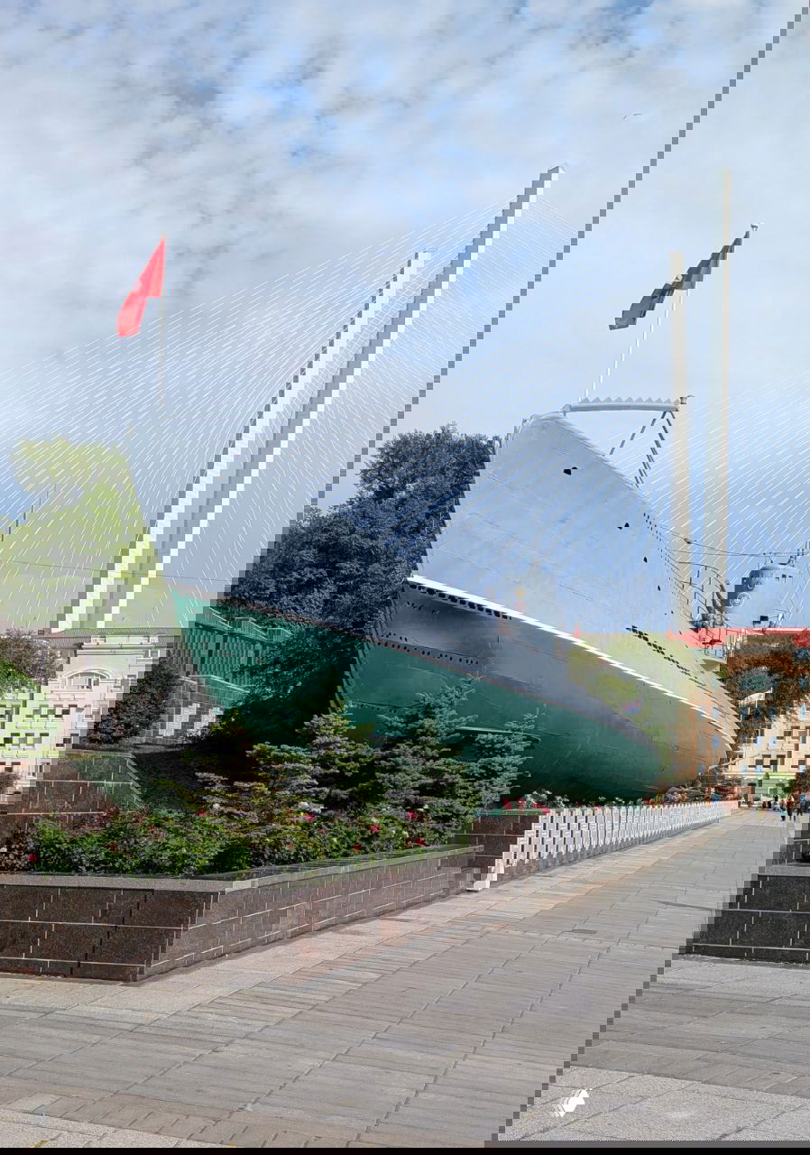 Носовая часть подлодки С-56 на пьедестале, на заднем плане виден современный мост — ракурс, демонстрирующий масштабы и окружение экспоната.