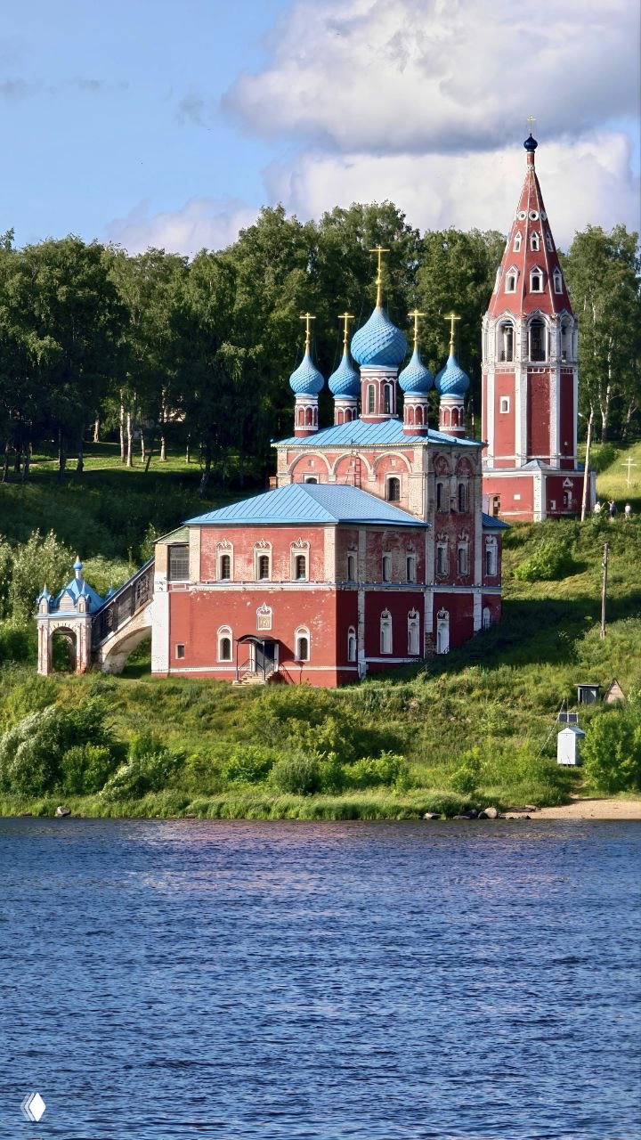 Казанско‑Преображенская церковь и отдельно стоящая колокольня у берега Волги: красные стены, синие луковичные купола и зелёный склон.