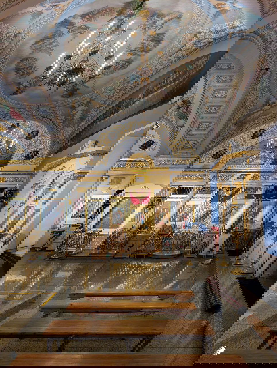 Интерьер храма с рядами скамеек и отражениями на полированном полу; на куполе видна фресковая роспись, создающая спокойную атмосферу для посещения.