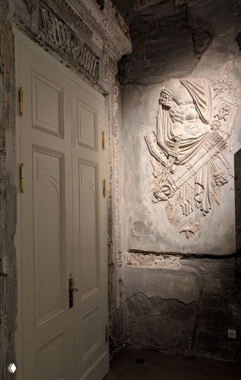 Открытая галерея с резными колоннами и оформлением второго яруса фасада дворца, видны архитектурные детали и отделка балконов на фоне серого неба.