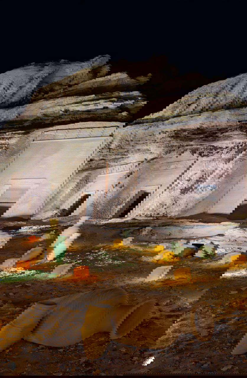 Оазисная зона с несколькими прямоугольными входами в скальные гробницы, внизу разложены глиняные амфоры и декоративные кубики-светильники.