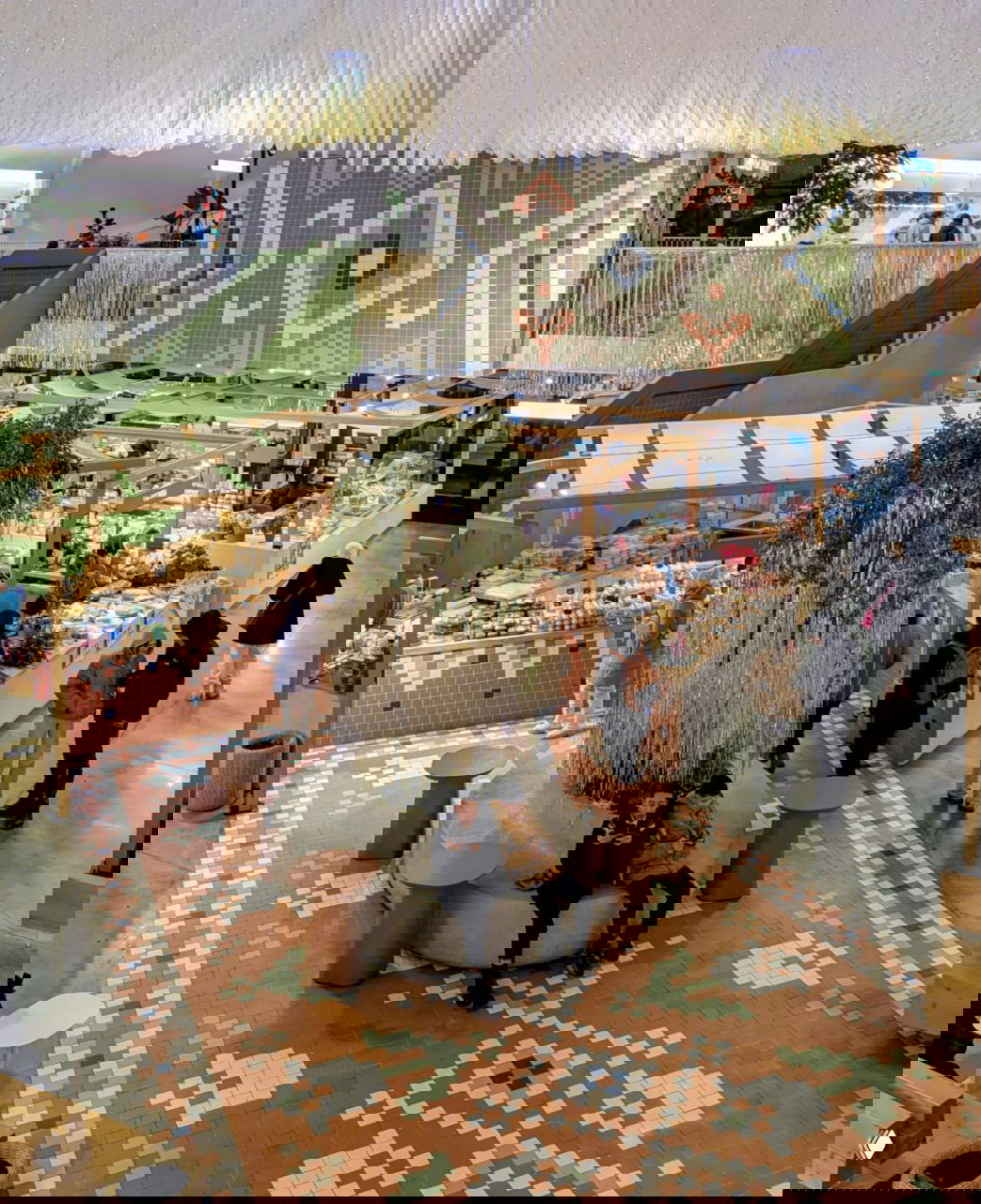 Внутренний вид торгового павильона Московского рынка: ряды прилавков, покупатели, декоративные растения и узорчатая мозаичная плитка на полу, вид сверху.