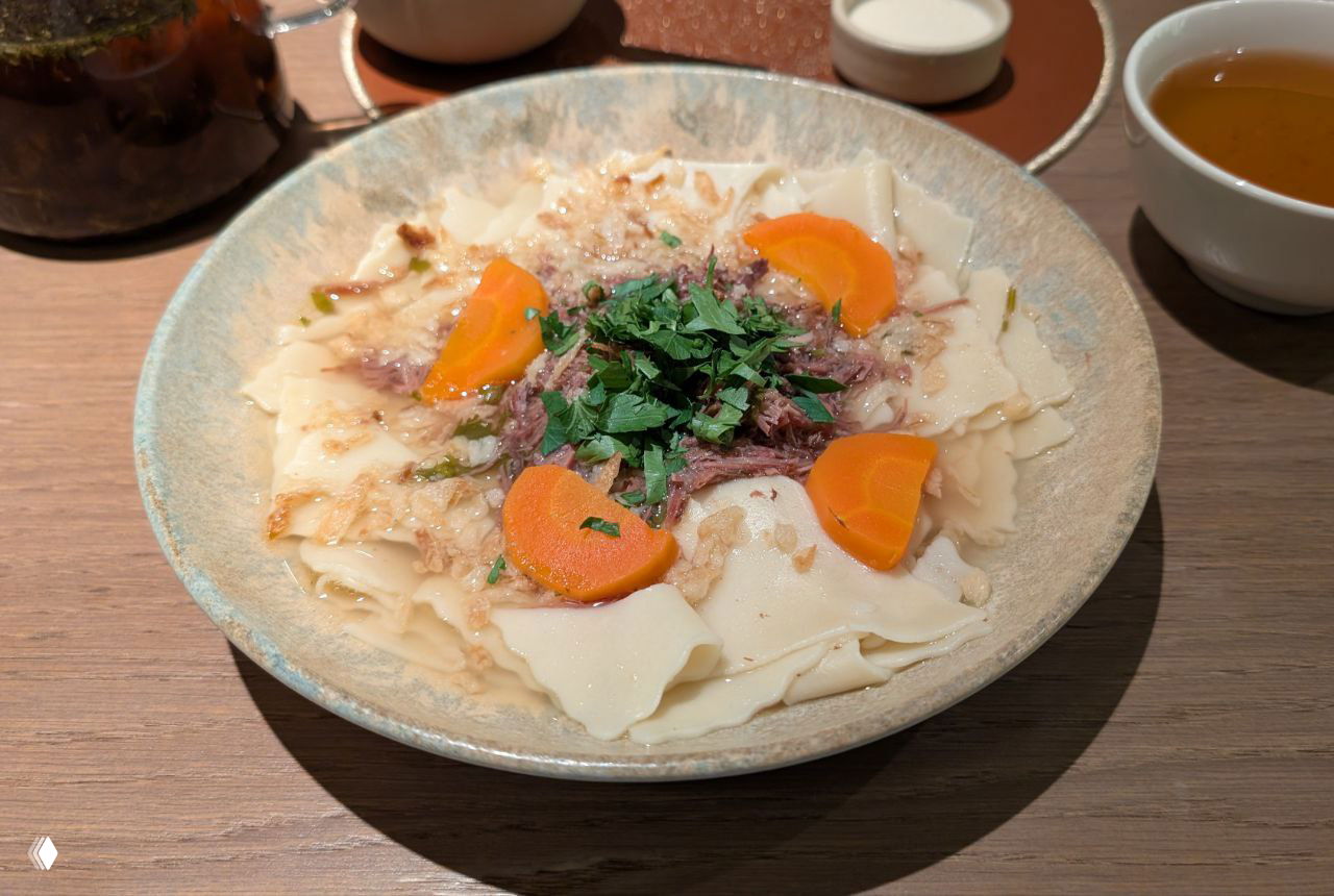 Большая миска с широкими пластинками теста, куском мяса в центре и нарезанной морковью — простое на вид, но сытное блюдо в авторской подаче.