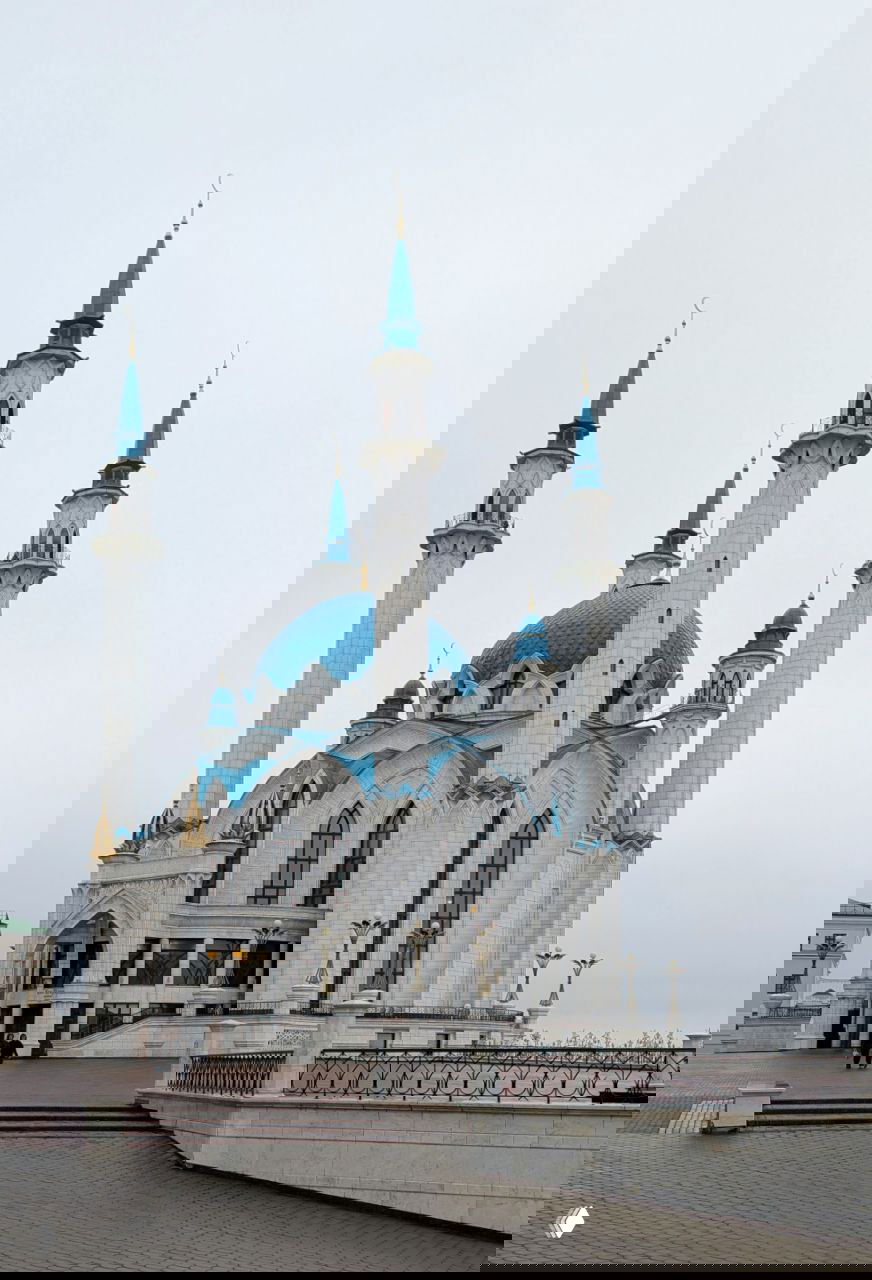 Дневной вид на мечеть Кул Шариф с подхода: белый фасад, голубые купола и минареты на фоне серого неба, лестница и ограждение кремля.