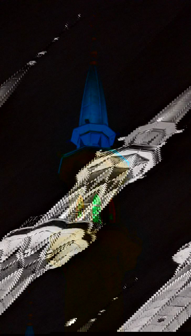 Крупный план верхней части минарета мечети Кул Шариф вечером: архитектурные детали, балкончик и освещённый купол на тёмном фоне.