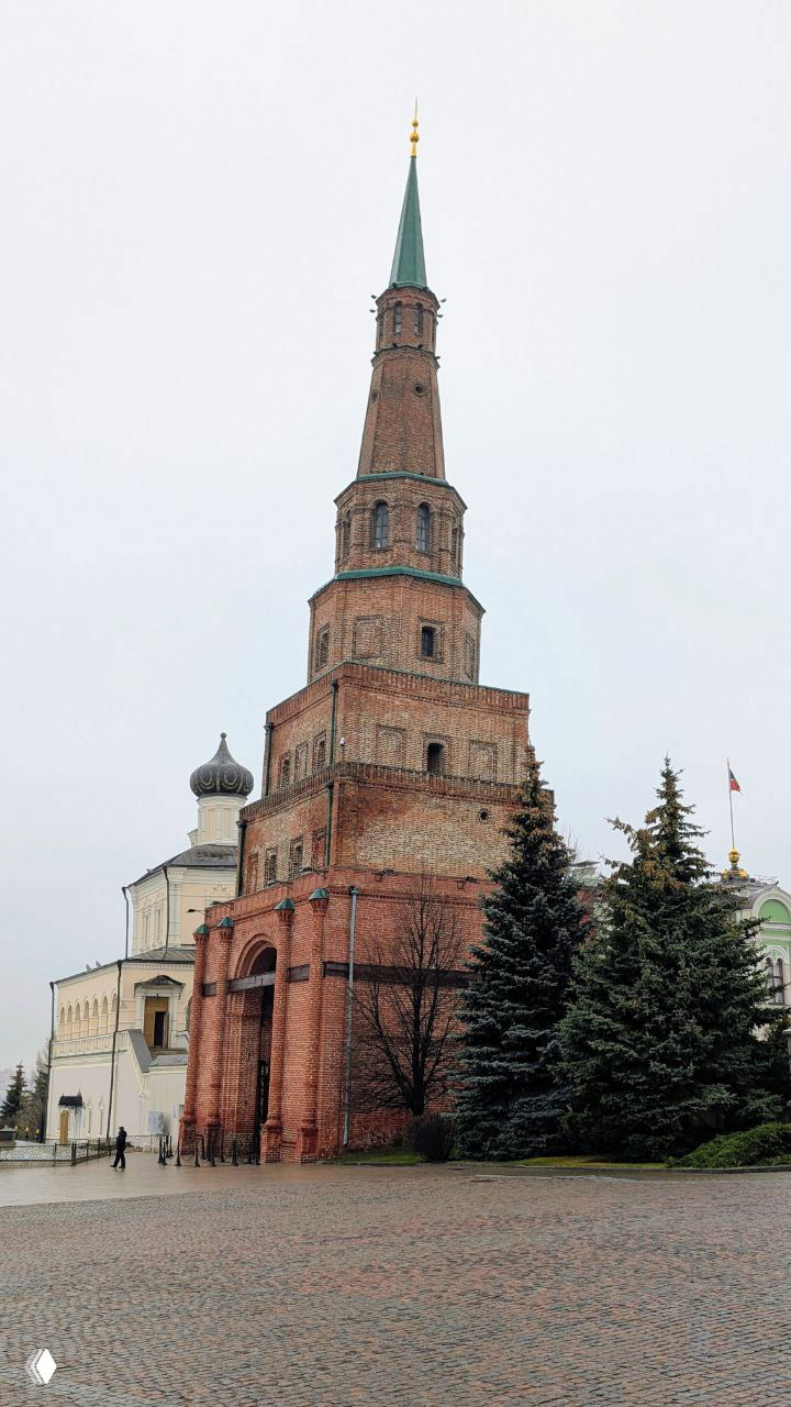 Высокая кирпичная башня Сююмбике в дневном свете на фоне пасмурного неба; масштаб и текстура кирпичной кладки хорошо видны.