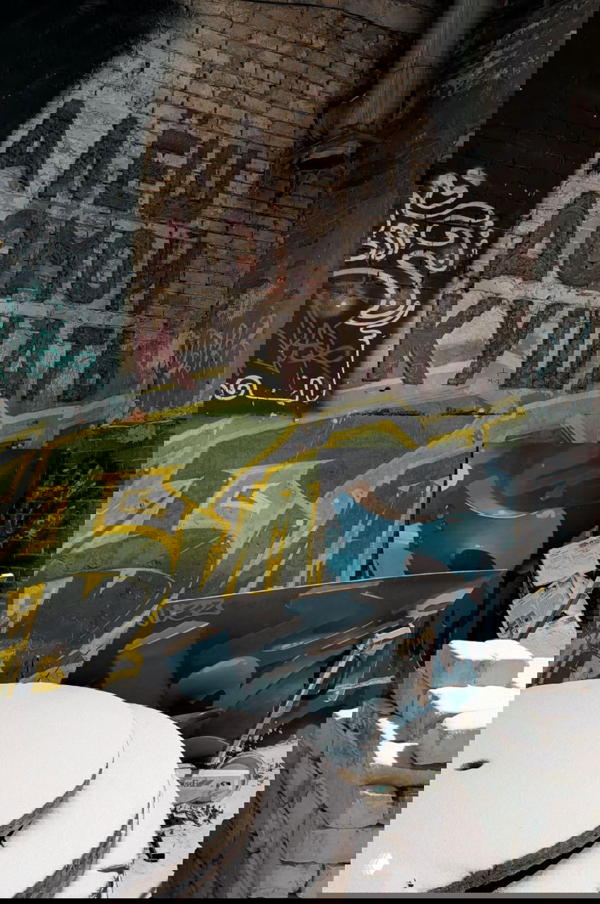 Внутренний двор с надписью «Алёш домой кушать» на кирпичной стене, строительные материалы и следы снега на земле в холодный вечер.