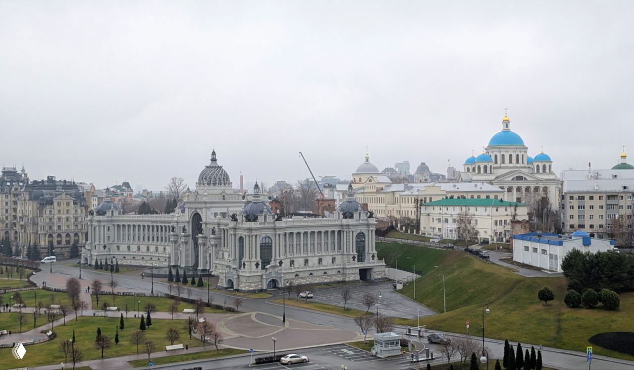 Панорамный вид на ансамбль Казанского кремля: Дворец земледельцев слева и Казанский собор с голубыми куполами справа под серым небом.