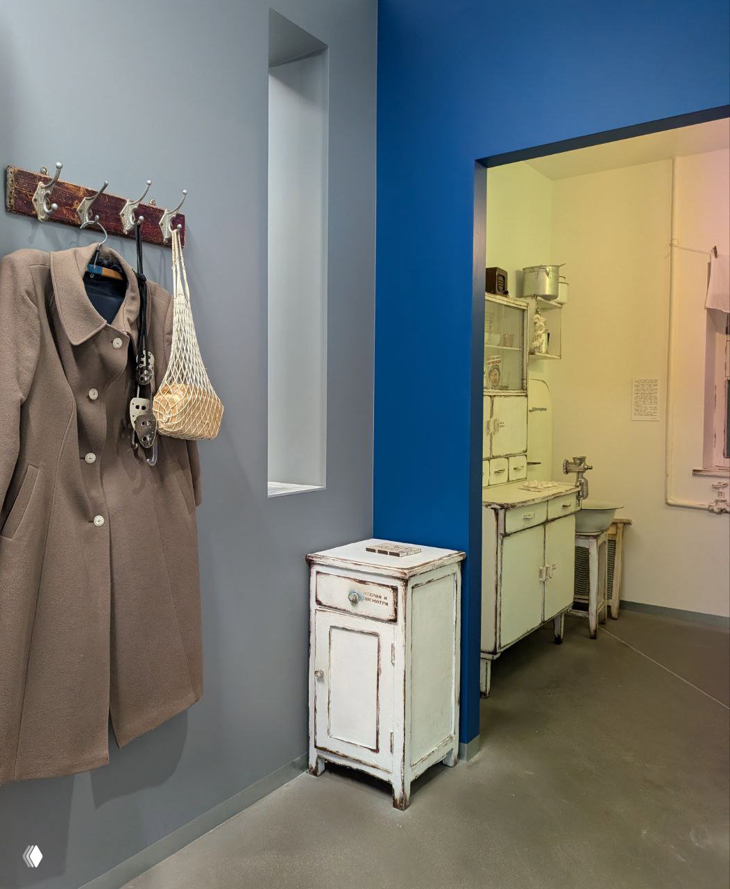 Угол экспозиции: вешалка с пальто и авоськой и вид в соседнюю кухню — сценография, отсылающая к быту фабричной столовой.