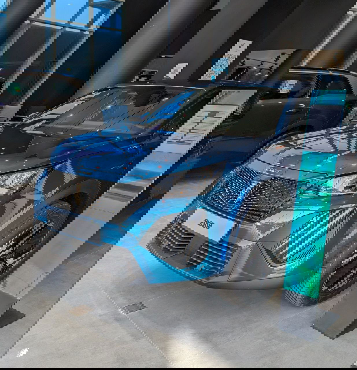 Синий кроссовер Peugeot 2008 выставлен в дилерском зале: видны передняя часть, номерная табличка модели и интерьер шоурума.