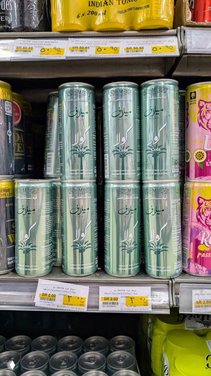 Стеллаж в супермаркете с зелёными банками финиковой колы "Миляф" и ценниками, крупный план упаковки и цен на полке.