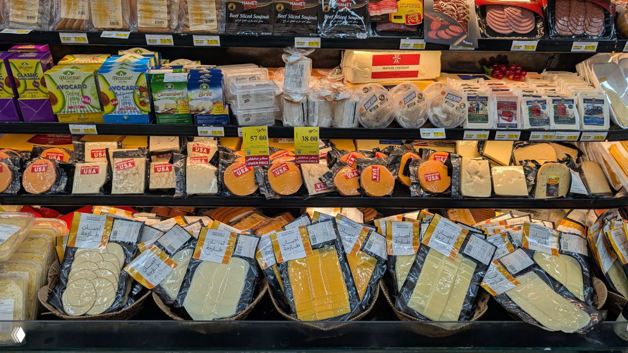 Витрина с упаковками сыра в супермаркете: нарезанные и брикетированные сыры, ценники и разнообразие импортных продуктов.