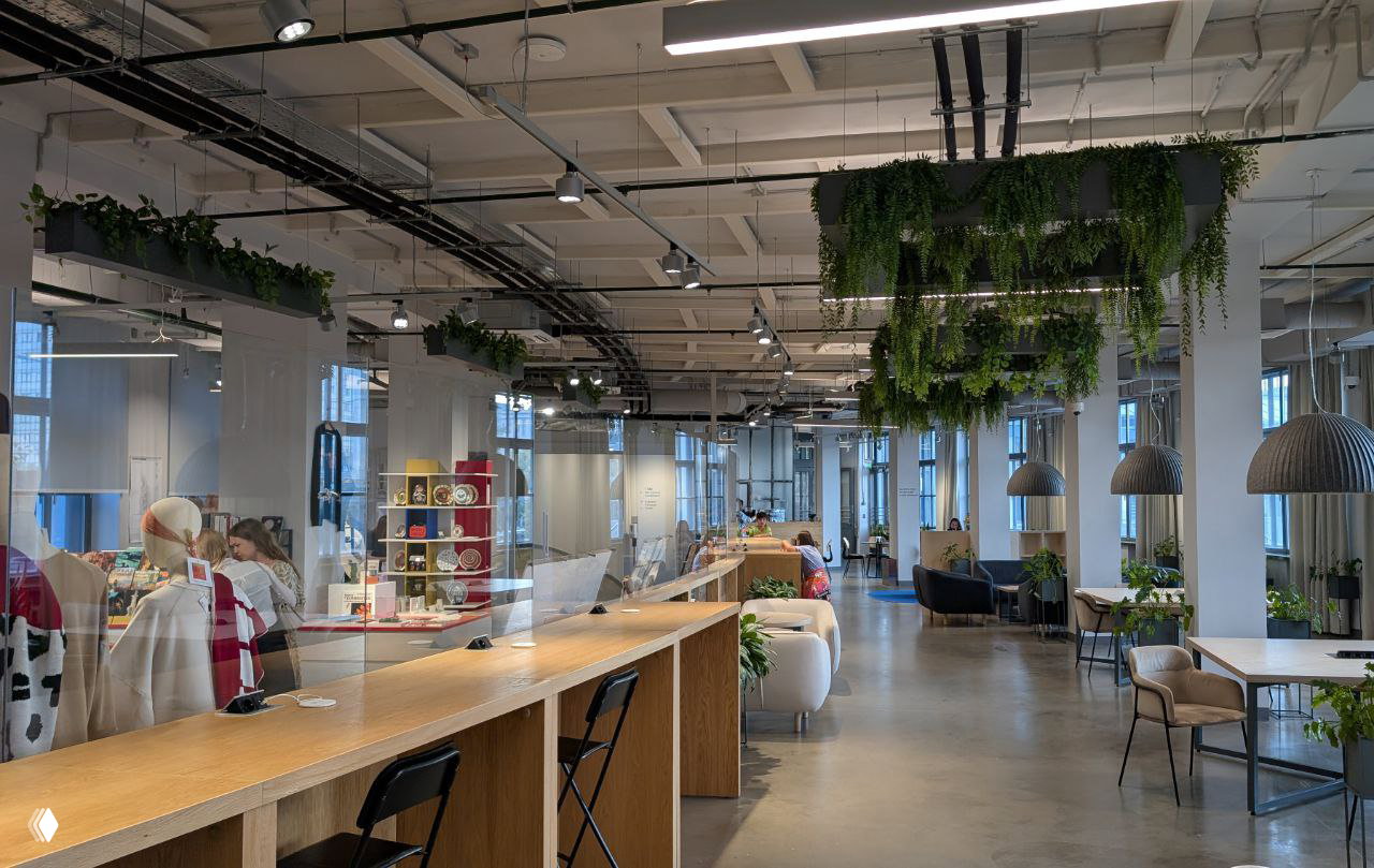 Просторный зал внутри филиала с длинными столами, подвесными растениями и зоной для посетителей и работы.