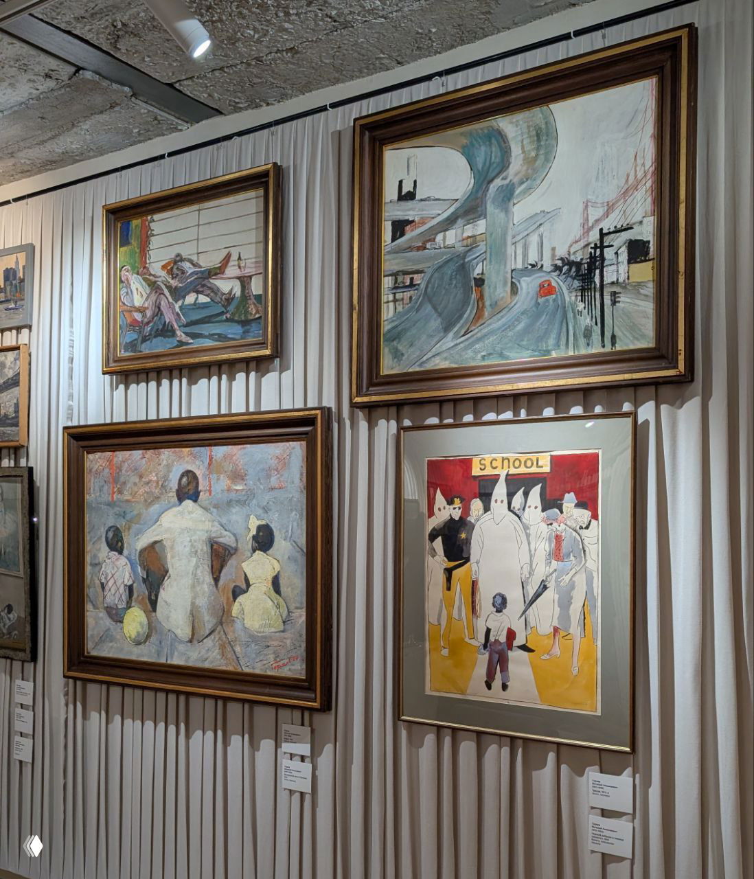 Стена с несколькими живописными полотнами в золоченых рамах: пейзажи и сценки, развешанные над текстильной занавеской, вид на яркую коллекцию работ разных авторов.