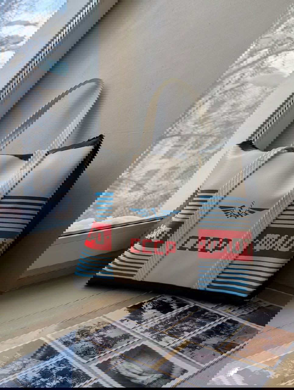 Ретро-сумка с надписью СССР на подоконнике и исторические черно‑белые фотографии под стеклом — предметы эпохи в музее, создающие атмосферу прошлого.