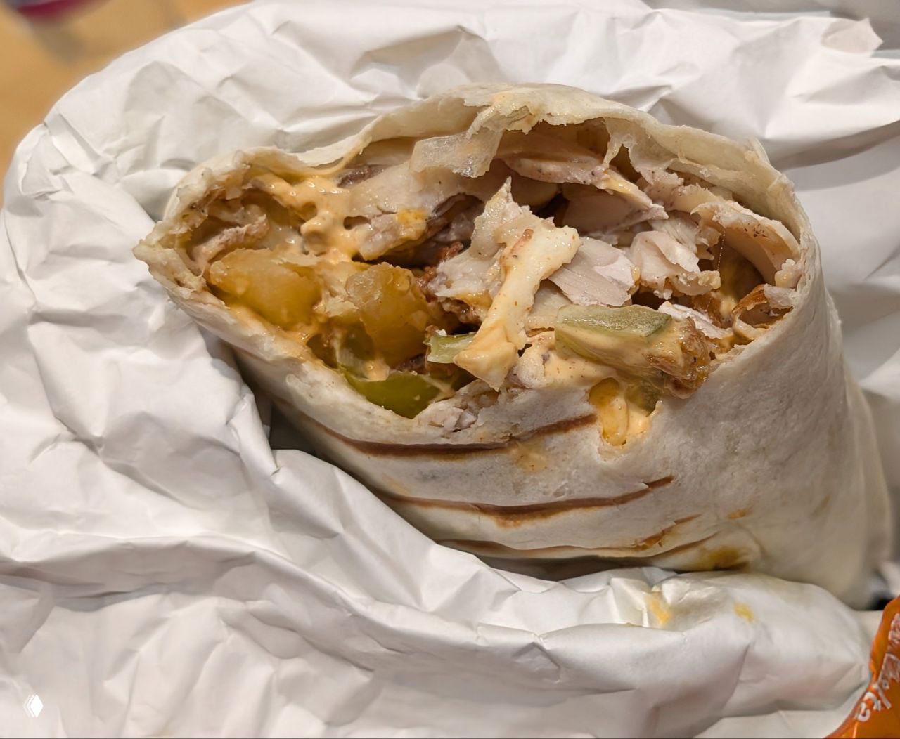 Крупный план разрезанной шаурмы в бумажной обёртке: видны мясо, маринованные огурцы и соус внутри лаваша.