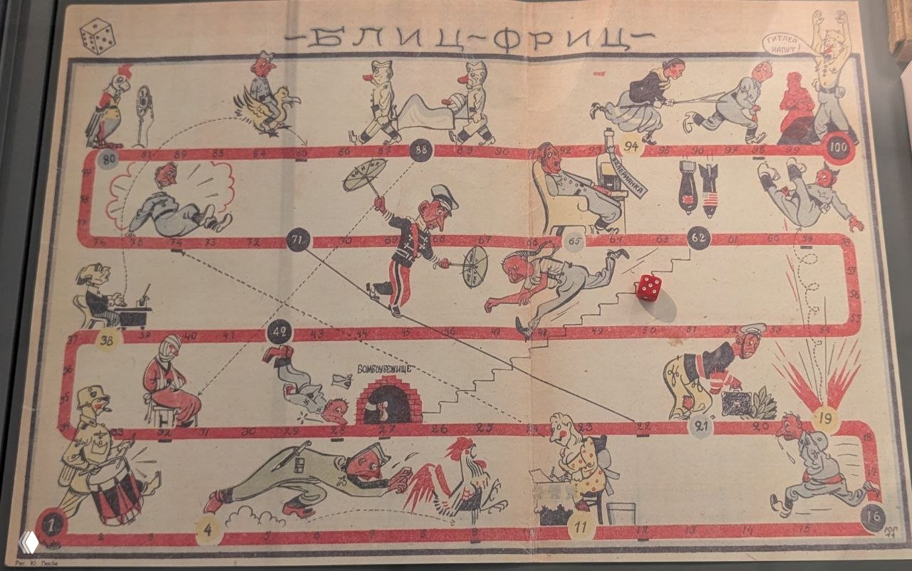 Игровое поле с карикатурами и сценами, экспонируемое как пример культурных артефактов и сатиры периода войны, демонстрирующее отношение к противнику.