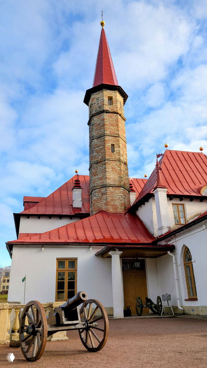 Кусочек дворца с кирпичной цилиндрической башней и старинной пушкой у входа — архитектура и военные экспонаты у парадного фасада.