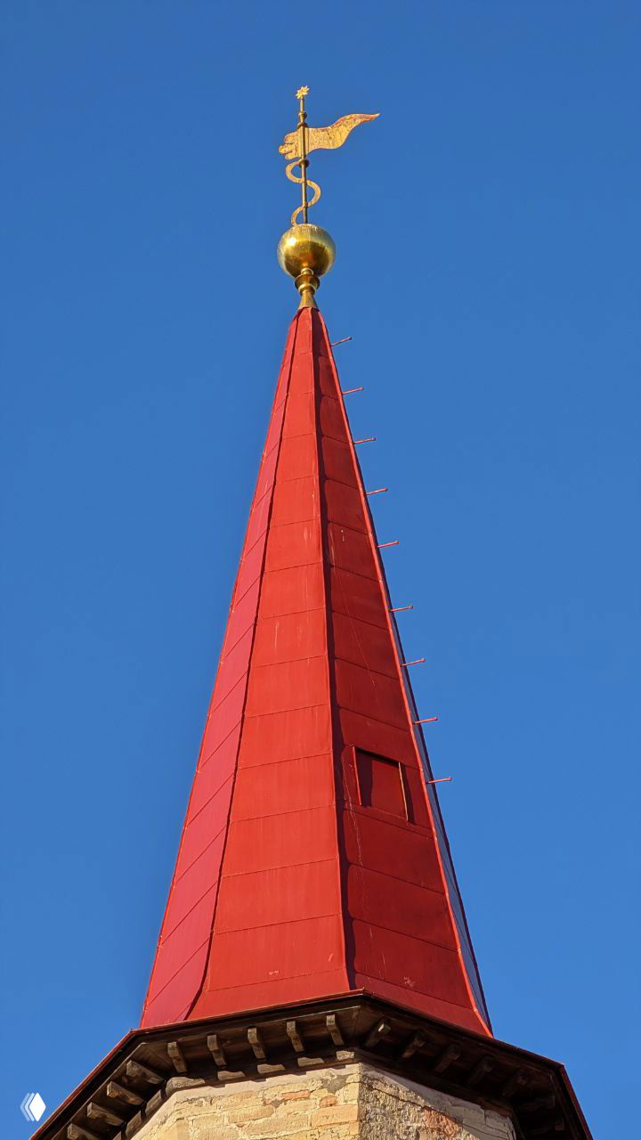 Крупный план острого красного шпиля с золотым навершием на фоне чистого синего неба — деталь декоративной кровли дворца.