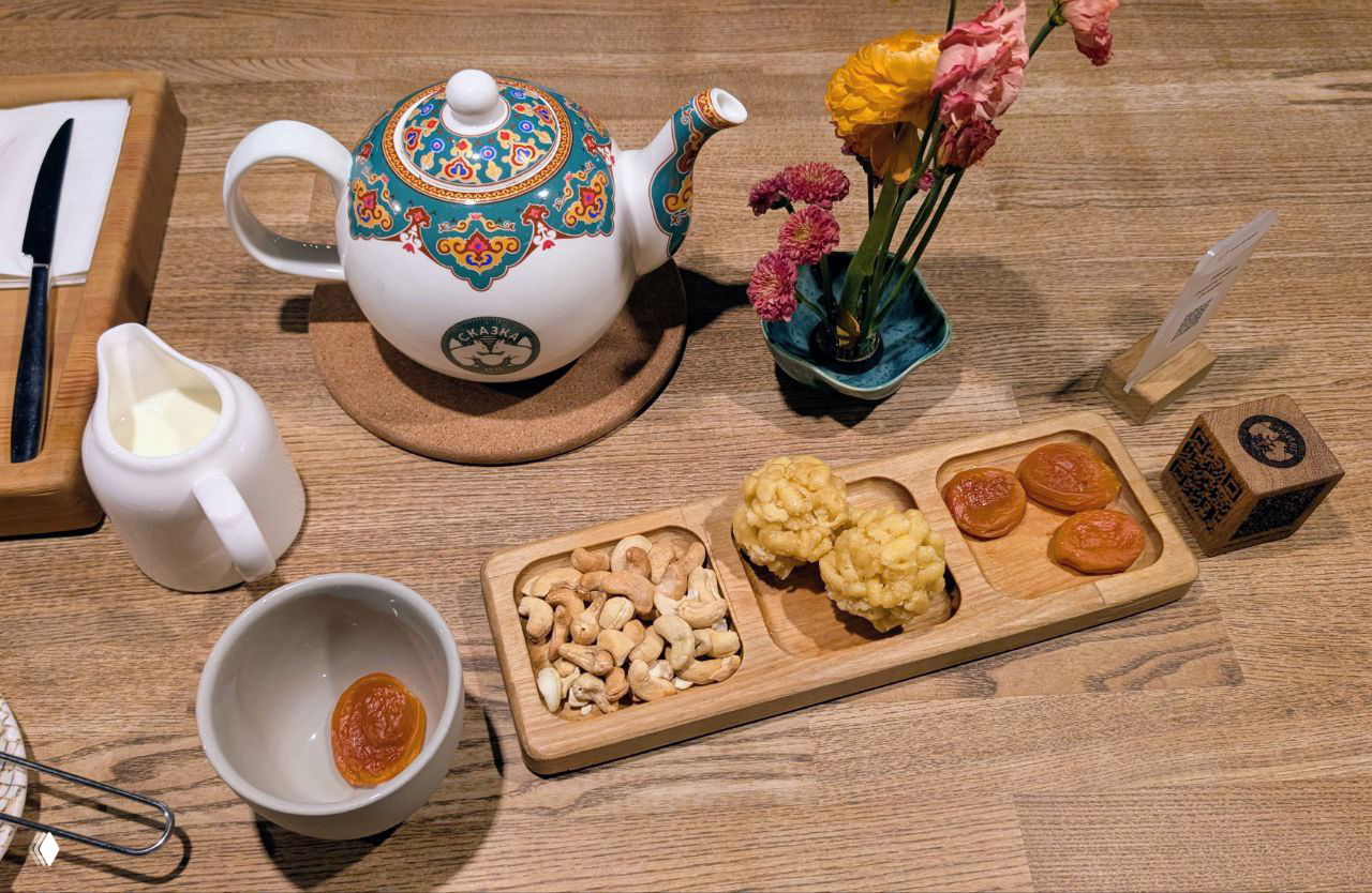 Чайник и поднос с угощениями: курага, орехи и традиционные сладости на деревянной тарелке, подача чая в ресторане Сказка рядом с музеем