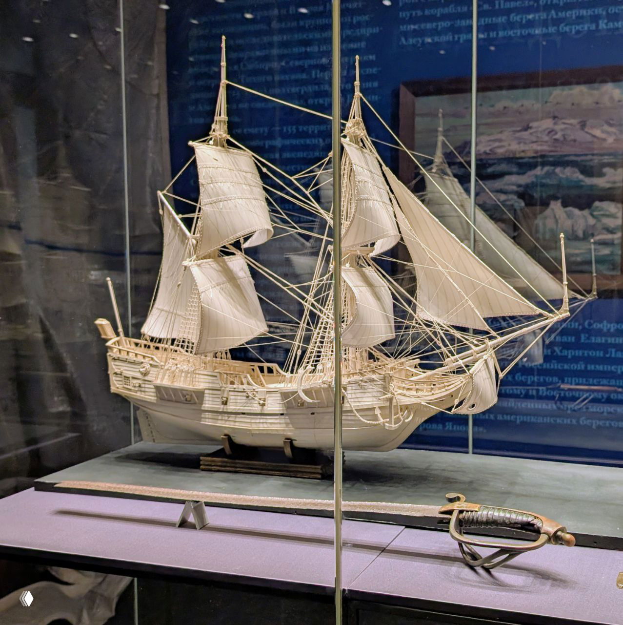 Модель парусного корабля в витрине экспозиции «Петр I. Северный ход», детализированная миниатюра с парусами и сопутствующей саблей на переднем плане.