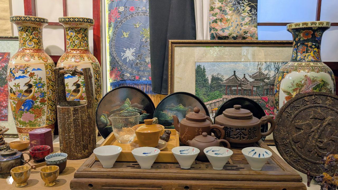 Коллекция чайной утвари: глиняные чайники и пиалы на подносе, декоративные вазы и плоские тарелочки в экспозиции, акцент на китайские предметы