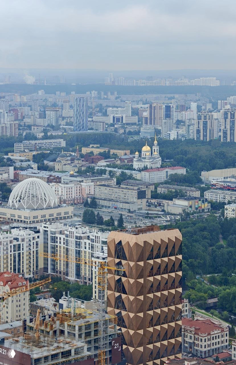 Широкая панорама городской застройки: современные высотки, купола храмов и заметное офисное здание «ананас» на фоне горизонта.
