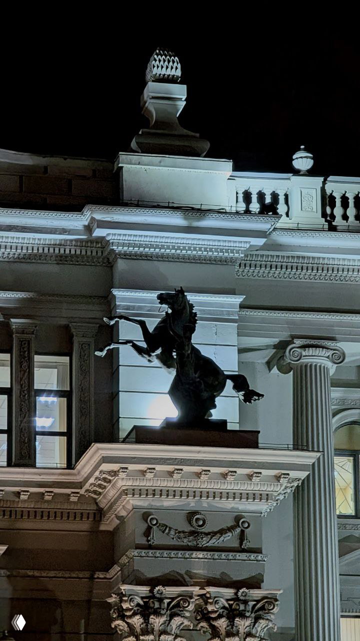 Скульптура скачущего коня на угловом фоне фасада Дворца земледельцев; вид подчёркивает монументальные элементы декора.