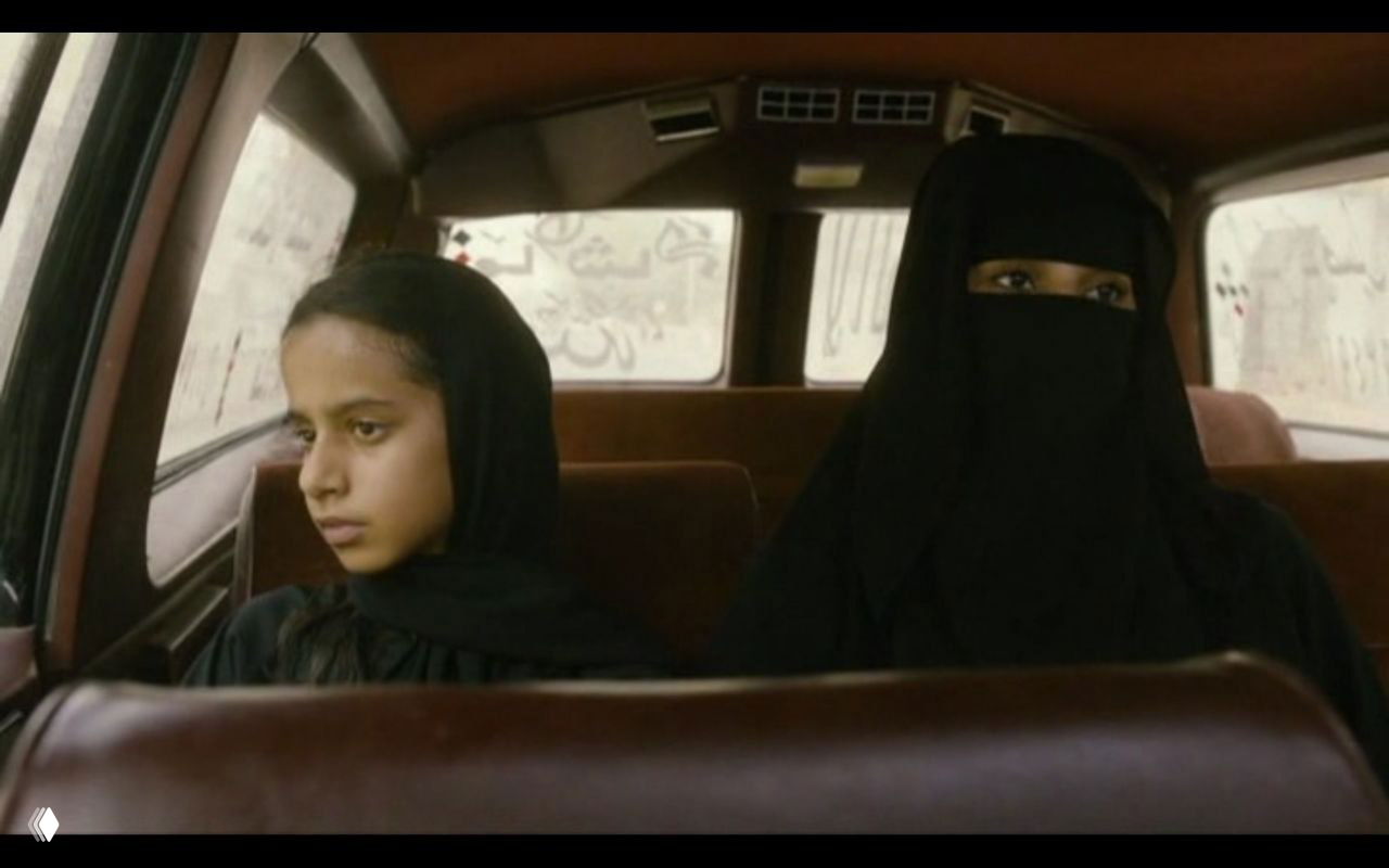 В салоне такси: молодая Ваджда и женщина в никабе молча едут по городу — кадр подчёркивает молчание и социальные роли героинь.