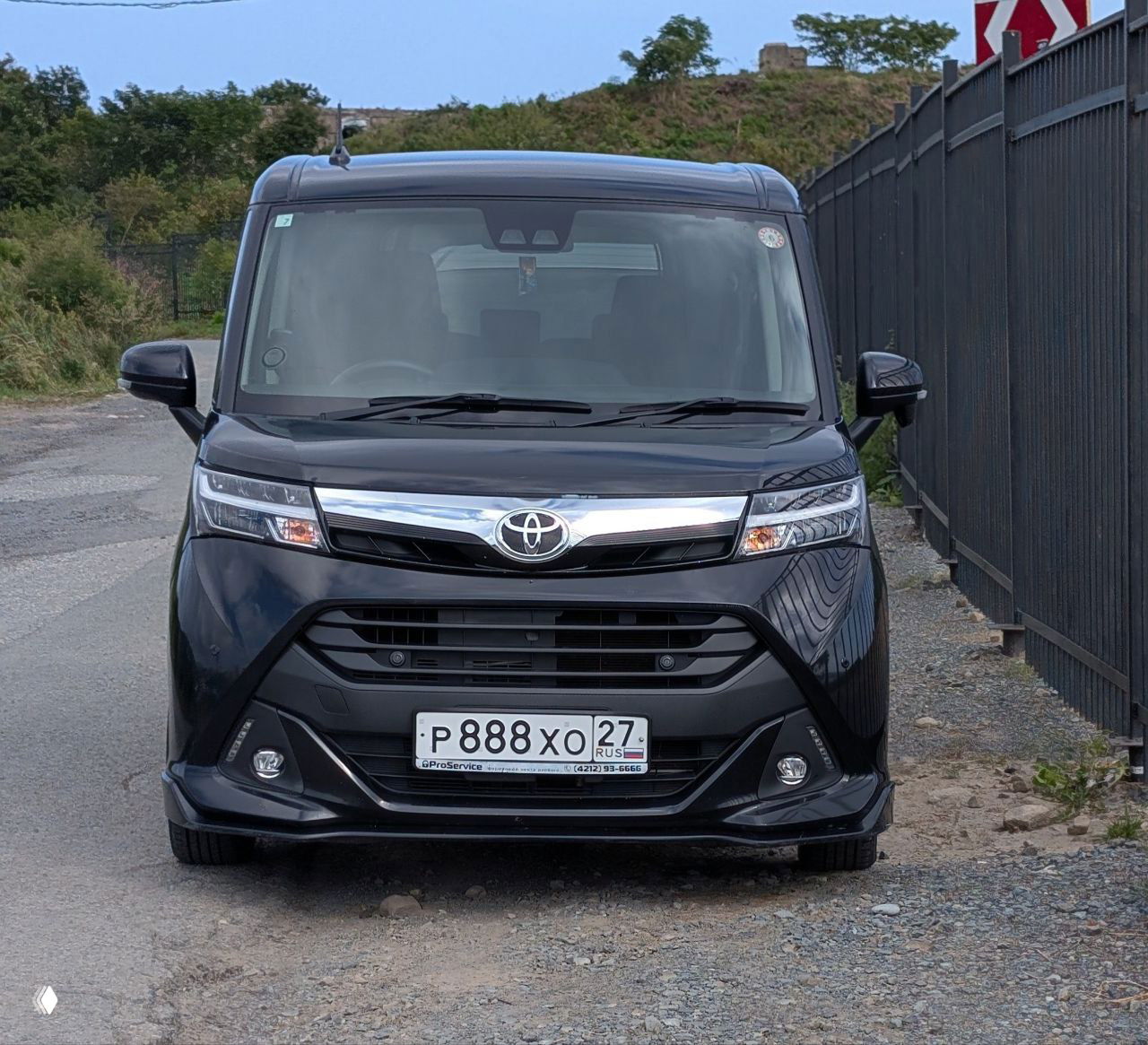 Чёрный минивэн Toyota Tank, снятый спереди на улице, автомобиль для аренды с дальневосточными номерными знаками, общий вид транспорта на стоянке.