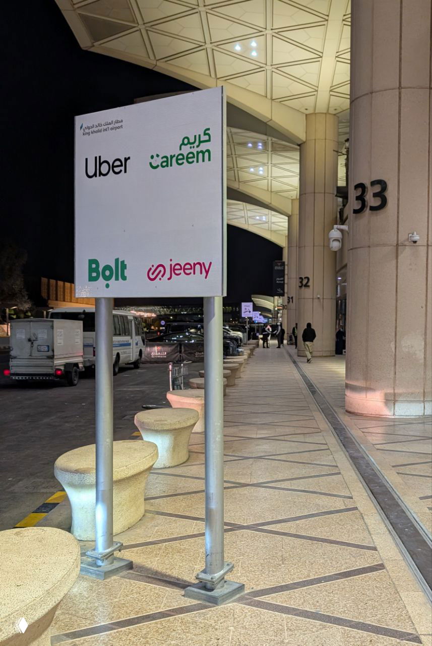 Ночной вид у аэропорта с указателем зон посадки такси (Uber, Careem, Bolt, jeeny) и тротуаром — визуал к разделу про трансферы.