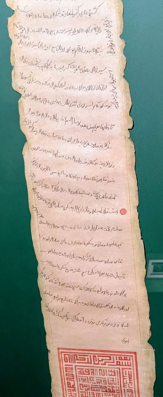 Свиток или рукопись с арабской и тюркской вязью на старом пергаменте в витрине музея, фрагмент официальных документов и грамот прошлых эпох.