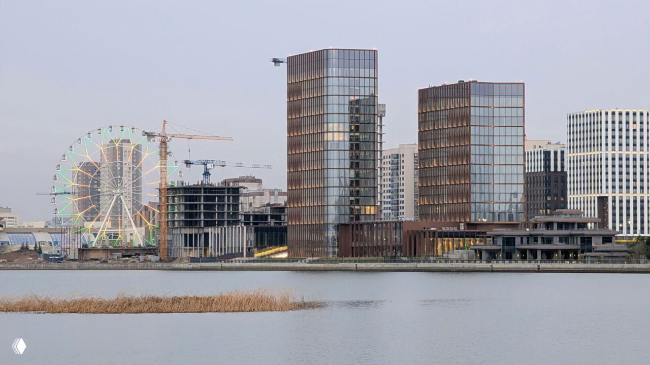 Современные жилые и офисные здания у берега Казанки с колесом обозрения и стройкой на фоне — пример новой городской застройки.