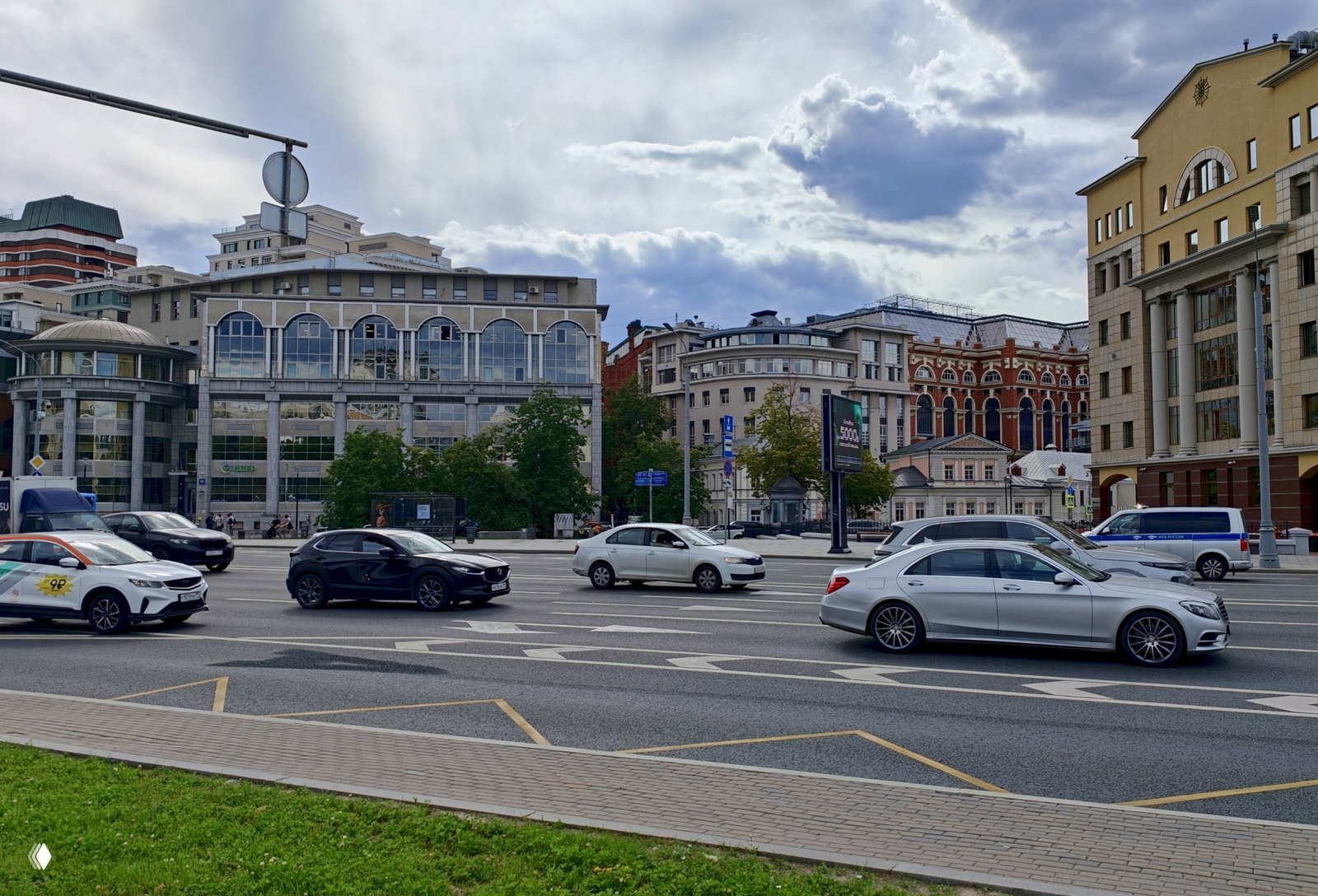 Вид на городскую улицу с интенсивным движением: автомобили, тротуар и фасады зданий в районе центра Москвы под облачным небом