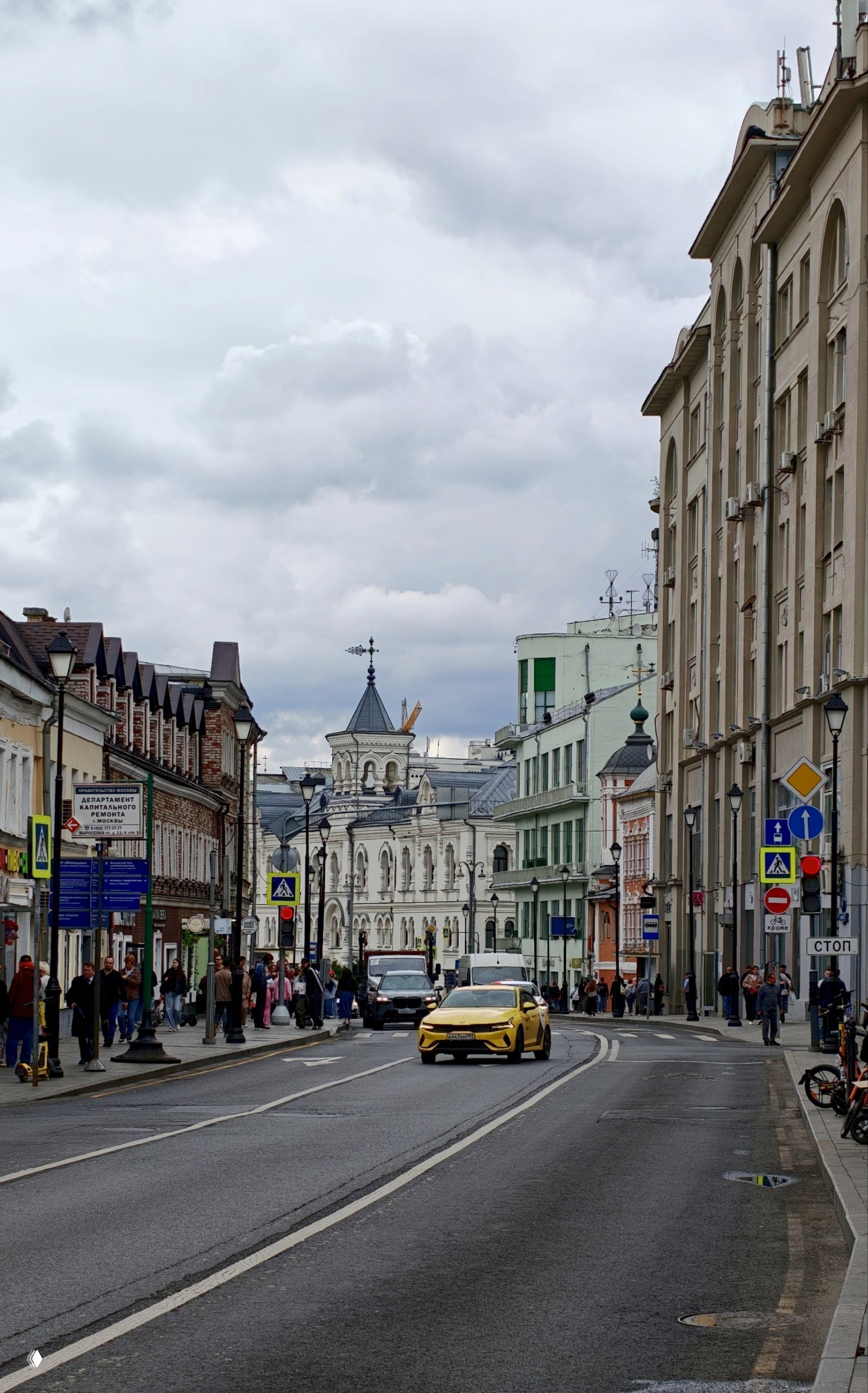 Узкая городская улица в центре Москвы со старинной архитектурой, пешеходами и желтым такси на переднем плане