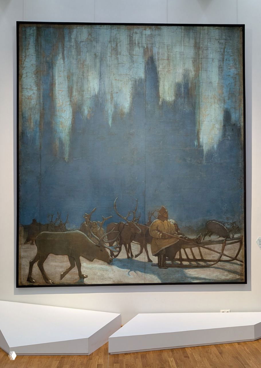 Картина с оленями и каюром у саней на холодном голубом фоне; крупное полотно в раме, перед которым выставочные подиумы и музейная полоса пола.