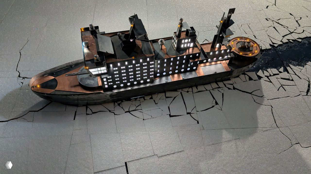 Макет или инсталляция корабля, размещённая на текстурированной «ледовой» поверхности с трещинами; подсветка подчёркивает форму судна.
